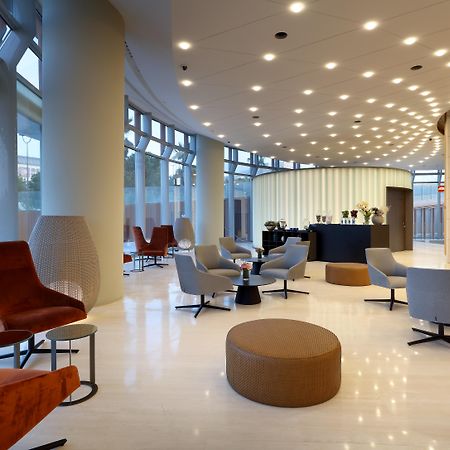 Eurostars Torre Sevilla Esterno foto The photo shows a modern, stylish lobby or lounge area. The design features a curved layout with large windows allowing natural light to flood the space. Various seating options are arranged throughout, including a mix of armchairs, lounge chairs, an
