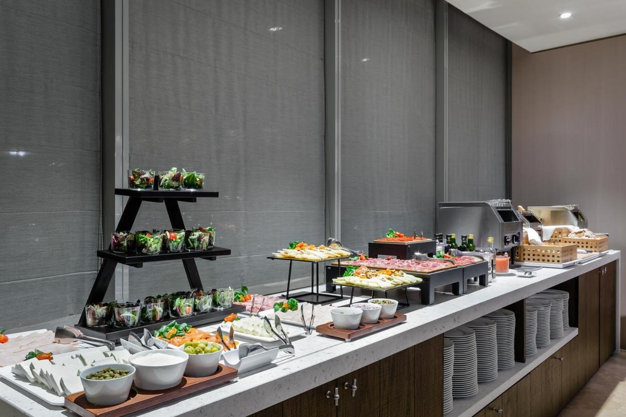 Eurostars Torre Sevilla Esterno foto The photo shows a buffet-style food display. There's a long countertop with various dishes arranged neatly. On the left, there are several small bowls and containers with salads, possibly garnished with fresh vegetables. In the center, there appears 