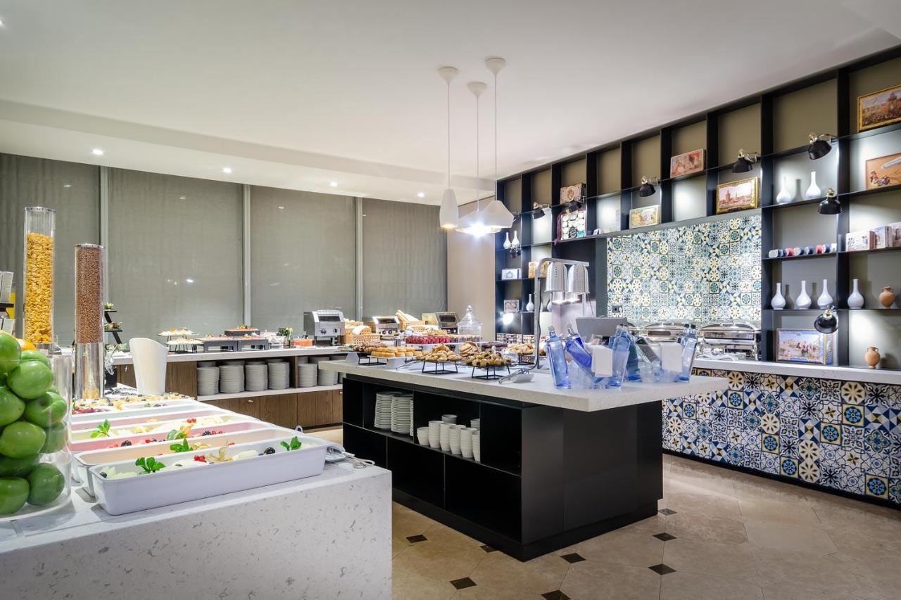 Eurostars Torre Sevilla Esterno foto The photo shows a modern buffet or dining area with a sleek design. There are multiple food stations, featuring a variety of dishes displayed on long tables. One table has bright, fresh-looking salads and ingredients, while another showcases desserts