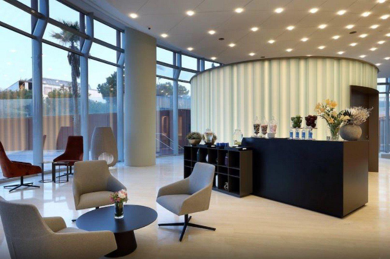 Eurostars Torre Sevilla Esterno foto The photo shows a modern reception area or lobby. It features large windows that let in natural light, creating a bright and inviting atmosphere. The interior design includes a mix of seating options, such as grey armchairs and a small black coffee t