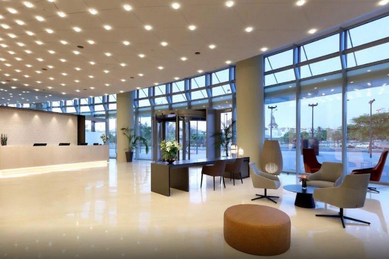 Eurostars Torre Sevilla Esterno foto The photo shows a modern reception area or lobby. It features a spacious and bright design with large windows that allow natural light to enter. The ceiling is adorned with numerous lights, enhancing the airy feel of the space. 

In the center, there