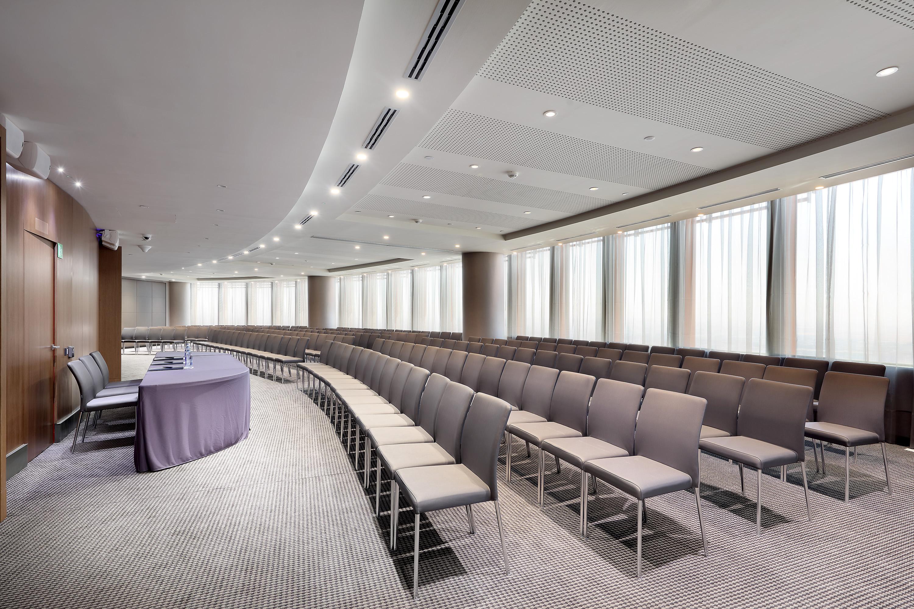 Eurostars Torre Sevilla Esterno foto The photo shows a conference room or meeting space designed for presentations or gatherings. There are rows of grey chairs arranged in a semi-circular layout, indicating a focus on a speaker or presentation area. At the front of the room, there is a 