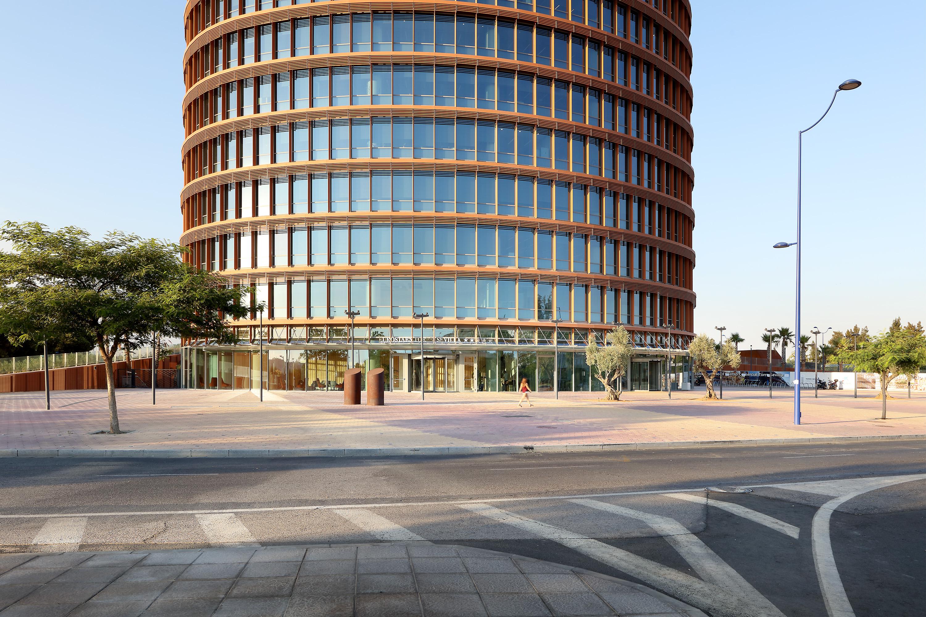 Eurostars Torre Sevilla Esterno foto The photo depicts a modern, multi-story building characterized by its round shape and large glass windows. The facade features a combination of glass and wood elements, giving it a sleek and contemporary appearance. In the foreground, there is an ope