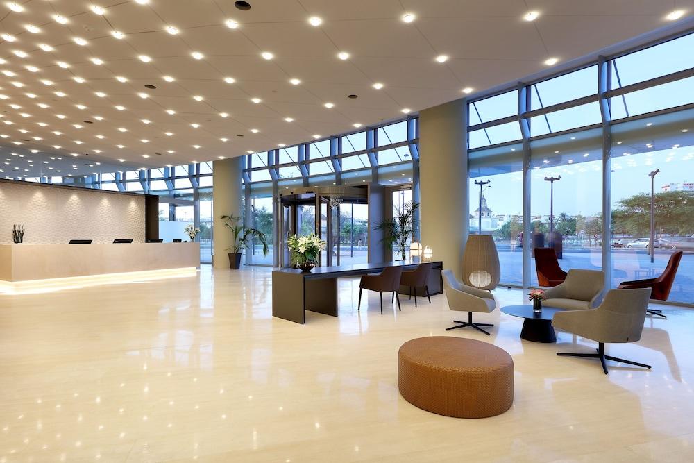 Eurostars Torre Sevilla Esterno foto The image depicts a modern reception area or lobby of a building. It features high ceilings and large windows that allow natural light to flood the space. The floor is polished and likely made of marble or a similar material, giving it a sleek appear