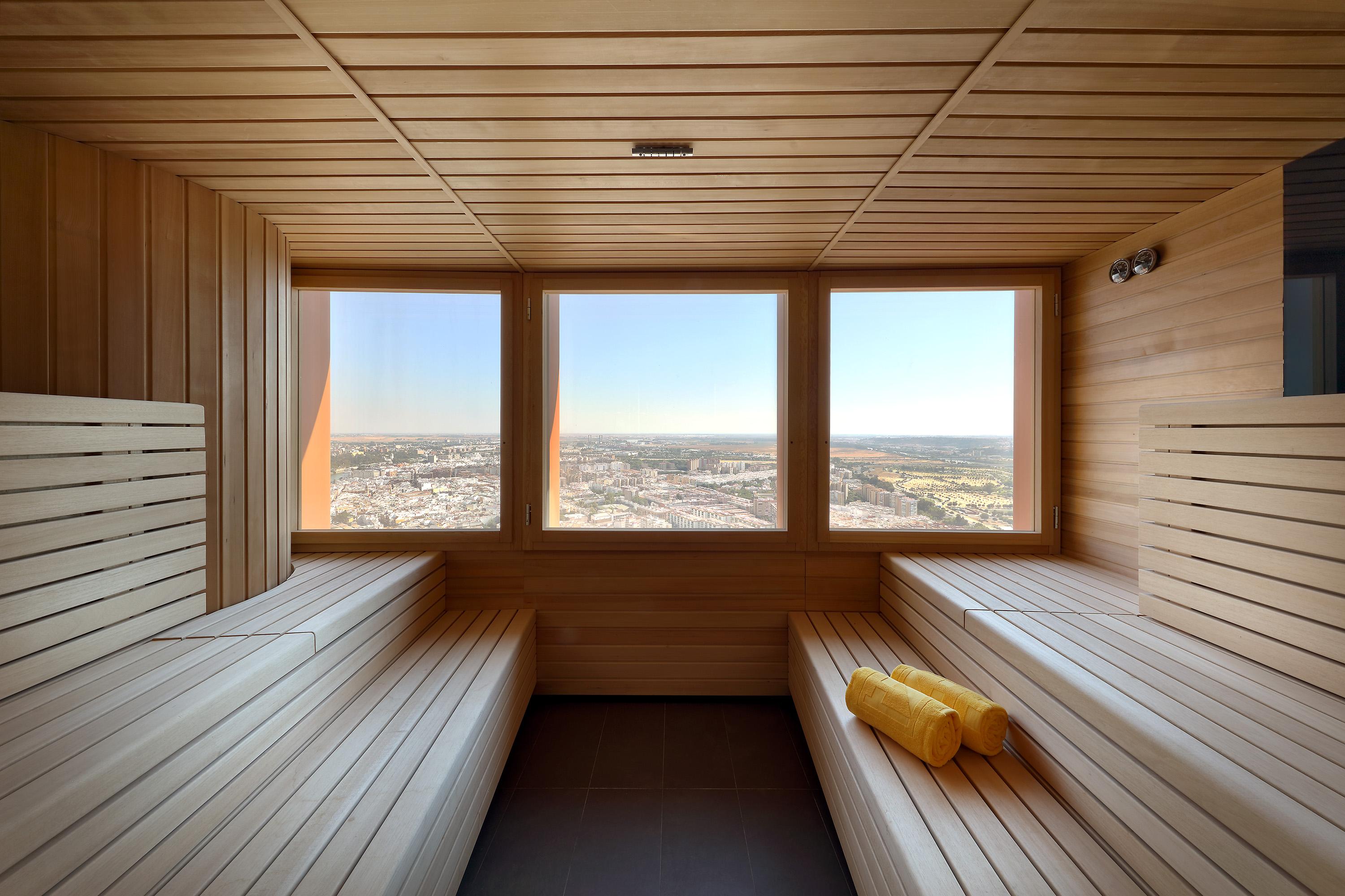 Eurostars Torre Sevilla Esterno foto The photo shows the interior of a sauna made primarily of wood. It features wooden benches arranged in a tiered setup, allowing for seating at different heights. There are large windows that provide a panoramic view of the outside landscape, showcasi