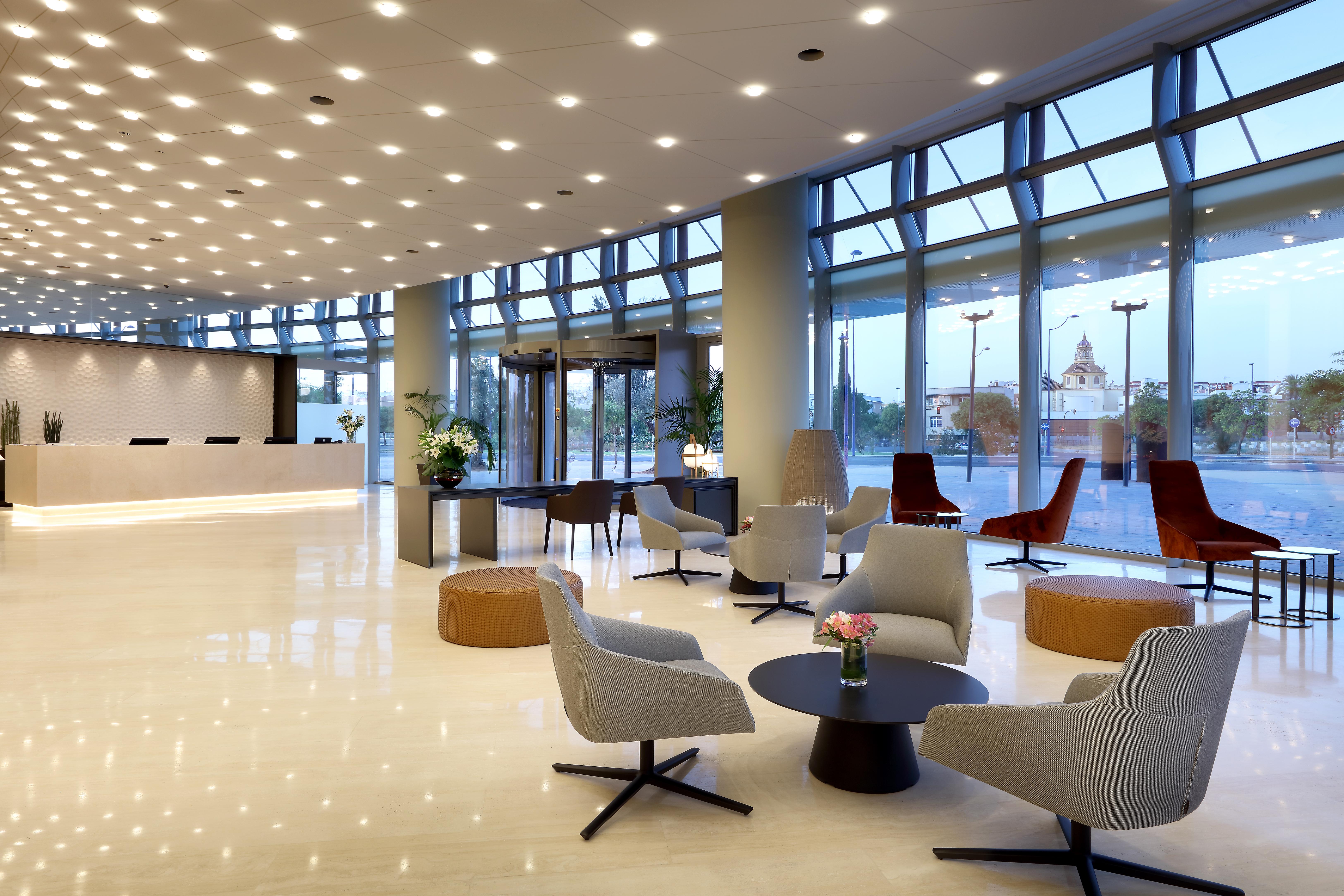 Eurostars Torre Sevilla Esterno foto The photo shows a modern lobby area with a bright, open layout. It features large windows that allow natural light to fill the space. The flooring is polished and light-colored, creating an elegant atmosphere. 

There are several seating arrangements