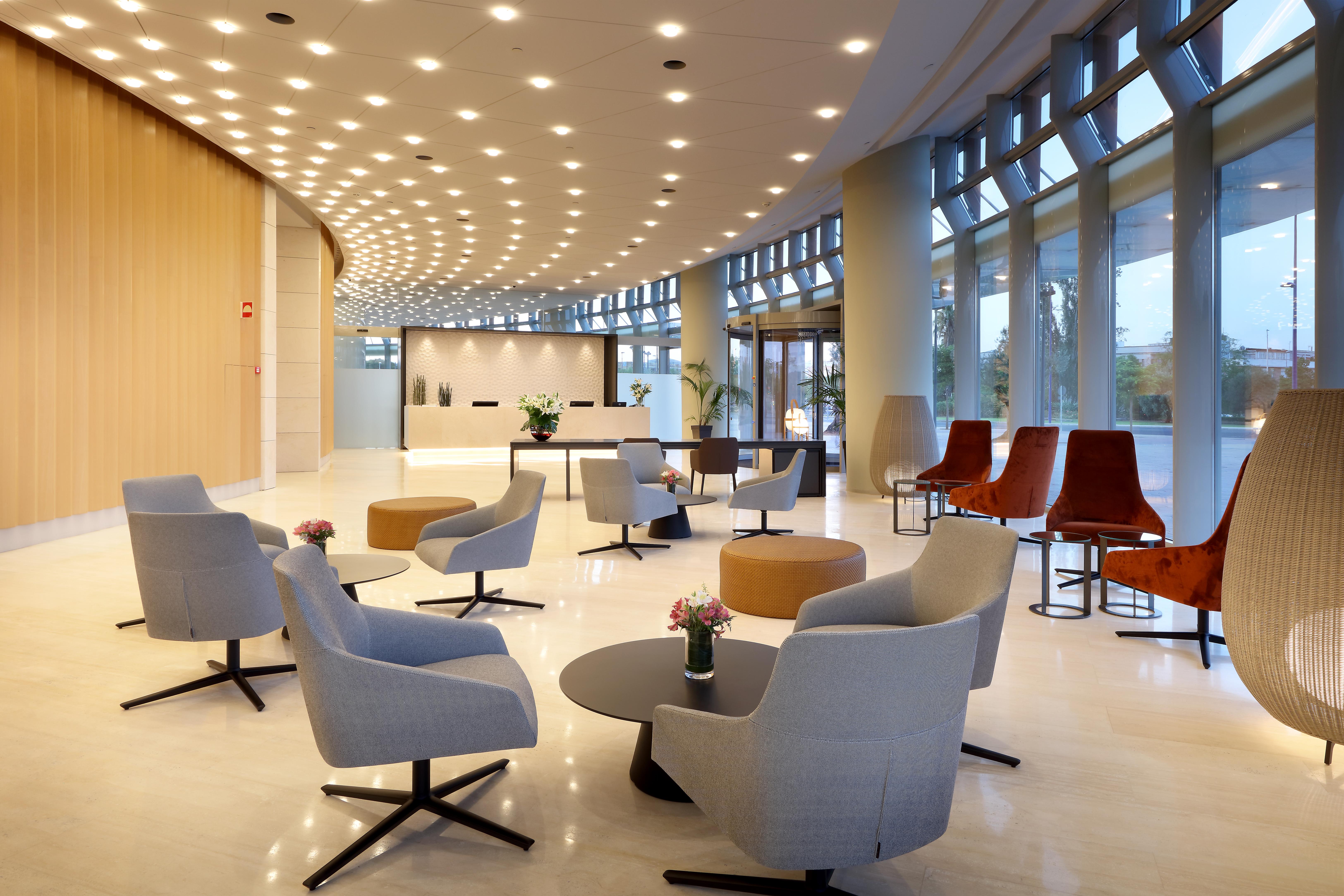 Eurostars Torre Sevilla Esterno foto The photo shows a modern lobby or reception area. It features a sleek design with a combination of chairs and tables arranged in a welcoming manner. The seating includes soft, light-colored armchairs and some darker, stylized chairs. In the center, t
