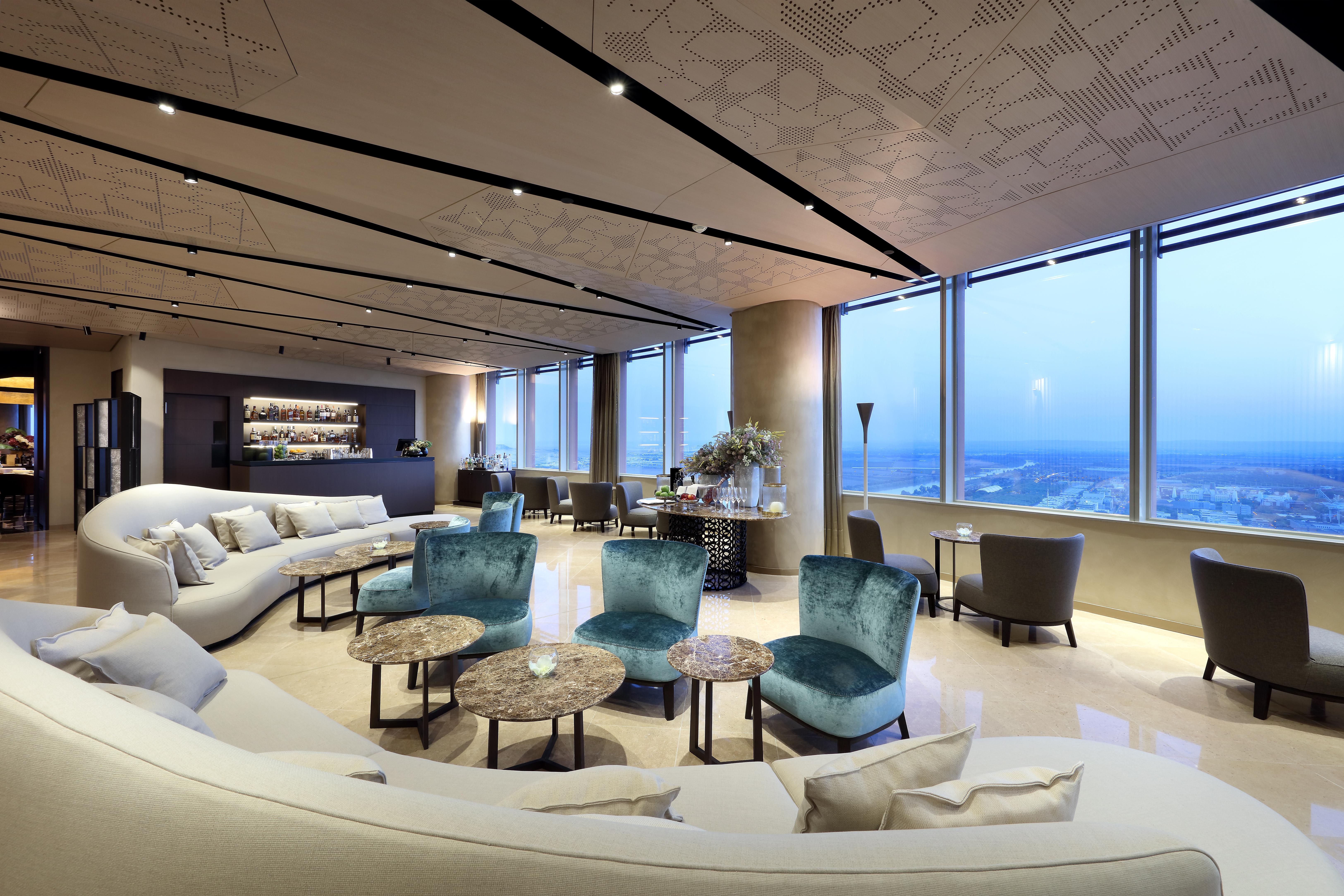 Eurostars Torre Sevilla Esterno foto The image shows a modern, upscale lounge area with large windows that provide a panoramic view of the city. The interior features a combination of elegant seating options, including a curved white sofa and several turquoise chairs around small marble