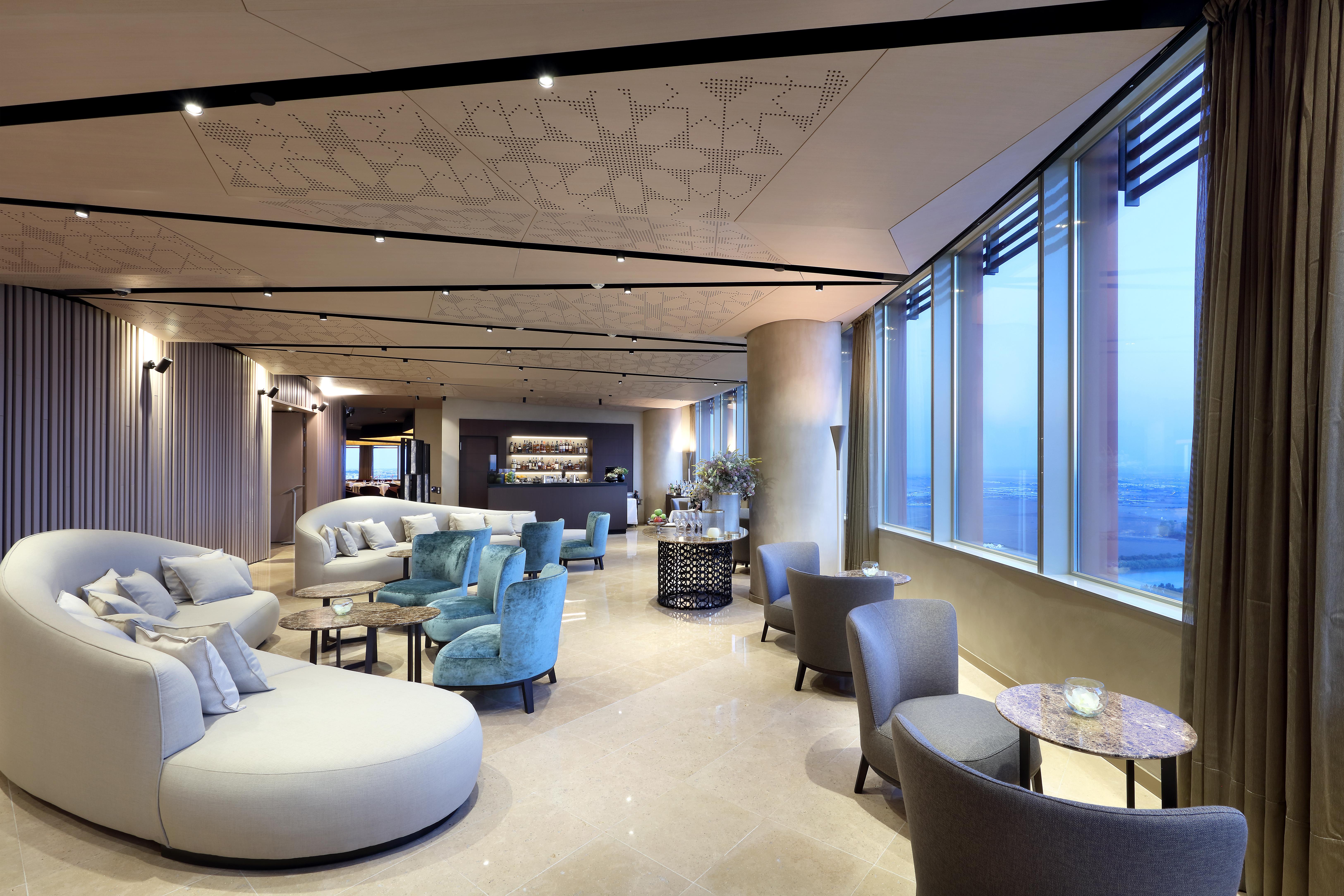 Eurostars Torre Sevilla Esterno foto The photo showcases a modern and stylish interior space, likely a lounge or waiting area. It features a combination of comfortable seating options, including curved white sofas and armchairs in light blue and gray tones. Large windows allow natural l