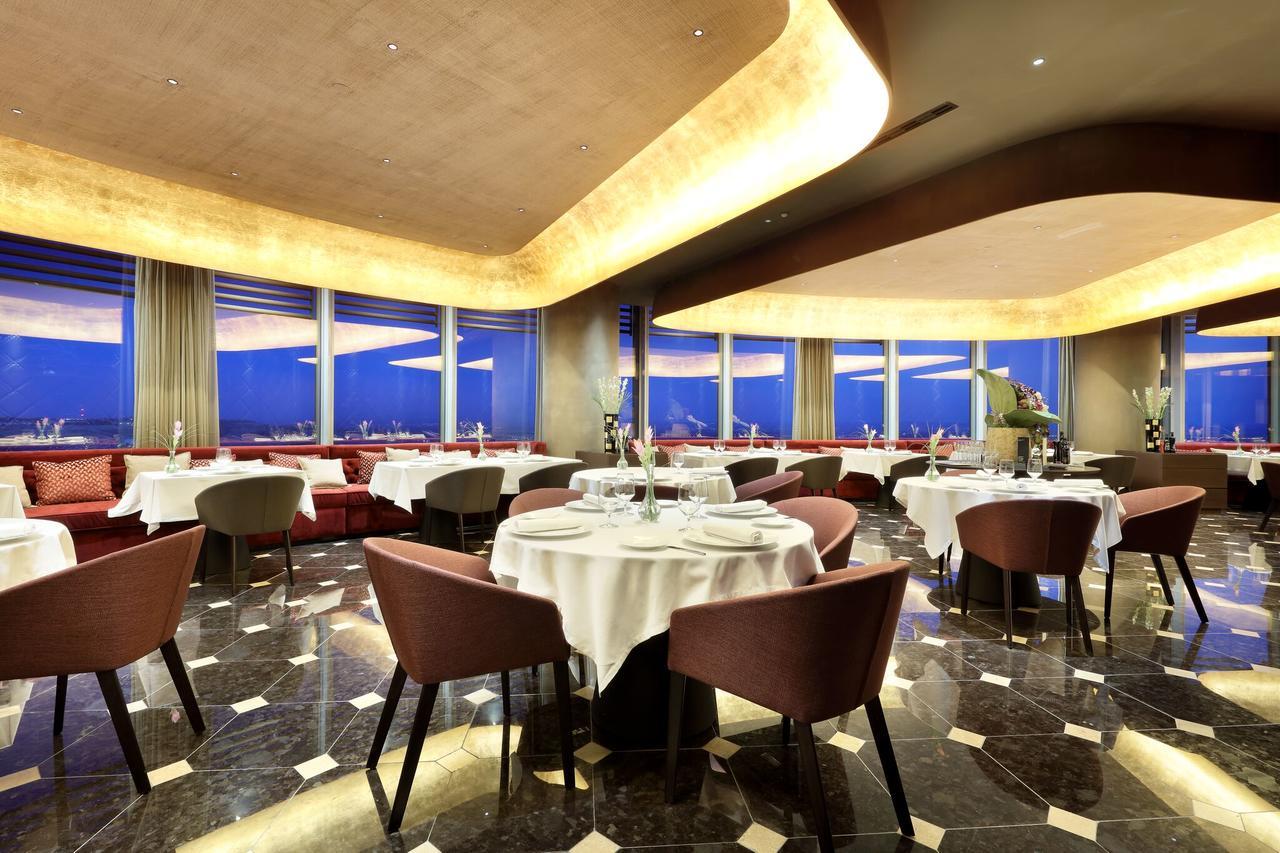 Eurostars Torre Sevilla Esterno foto The photo shows an elegant restaurant interior. It features modern decor with a sophisticated ambiance, including round tables covered with white tablecloths. The seating consists of stylish chairs, and large windows provide a view of the outside, li
