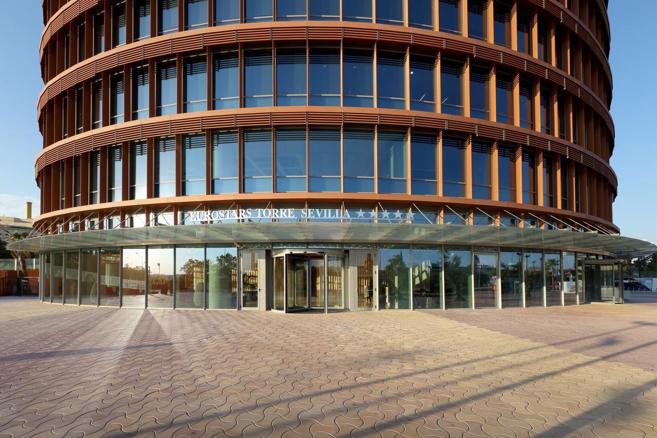 Eurostars Torre Sevilla Esterno foto The photo shows a modern building known as the "Cajasol Torre" located in Seville, Spain. It features a curved facade made of glass and metal, with multiple levels visible through large windows. The entrance is covered by a glass canopy, providing an