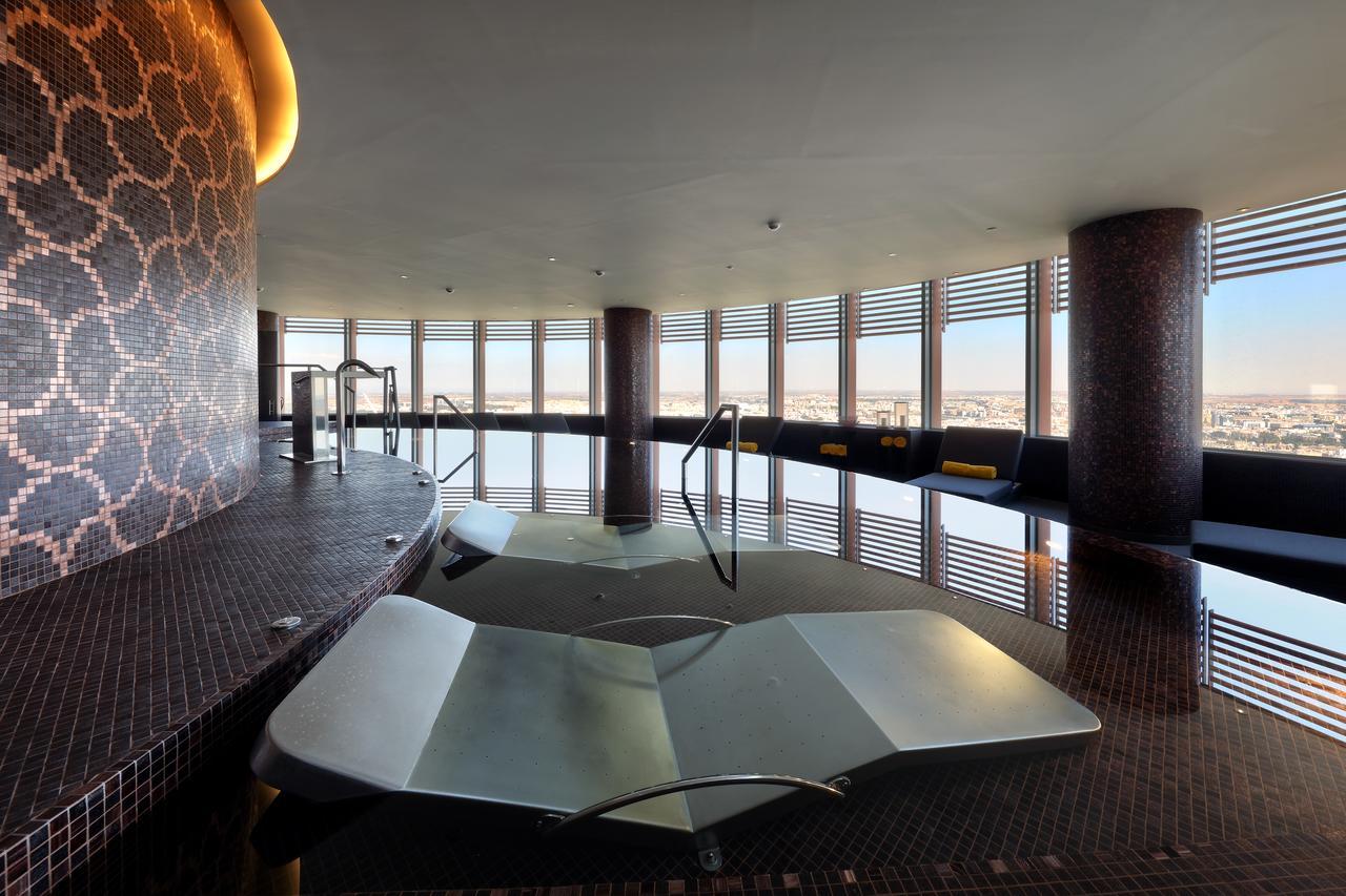Eurostars Torre Sevilla Esterno foto The photo depicts a modern spa or wellness area with large windows offering a panoramic view of the surroundings. In the foreground, there are two sculptural lounge areas that appear to be partially submerged in water. The interior features elegant t