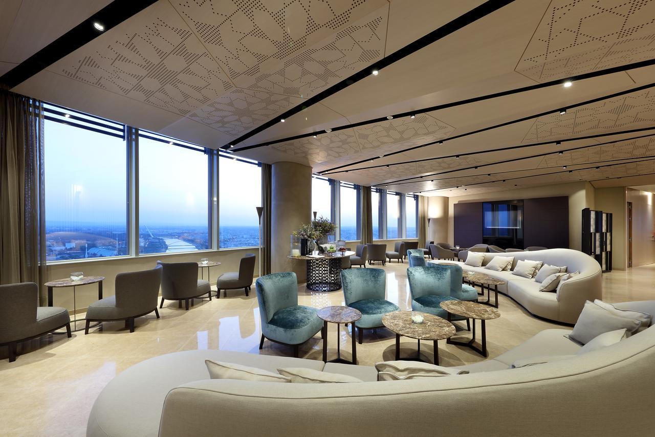 Eurostars Torre Sevilla Esterno foto The photo shows a modern, elegantly designed lounge or lobby area. It features large windows that provide expansive views of the landscape outside, allowing natural light to fill the space. The interior design includes a combination of soft, curved f