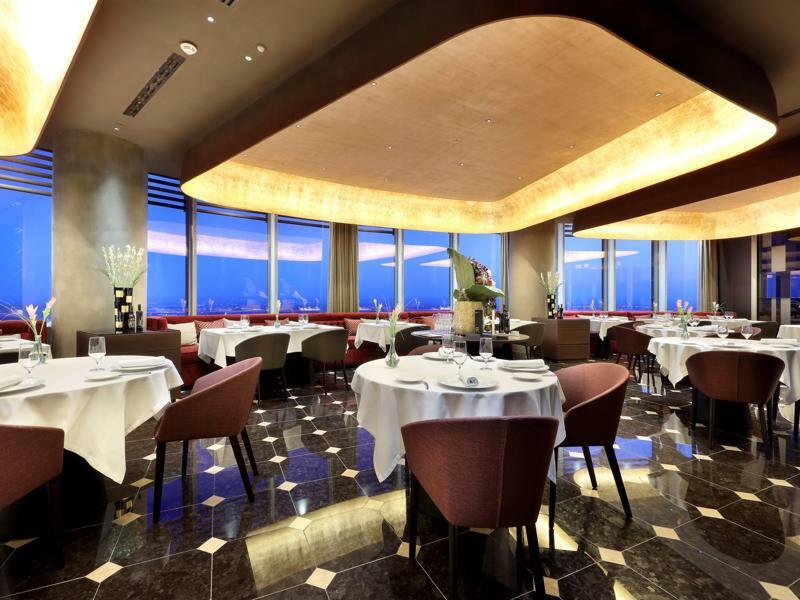 Eurostars Torre Sevilla Esterno foto The photo depicts a modern, upscale restaurant with an elegant interior design. The dining area features round tables, each set with white tablecloths and elegant dishware, indicating a fine dining atmosphere. The walls are adorned with large windows
