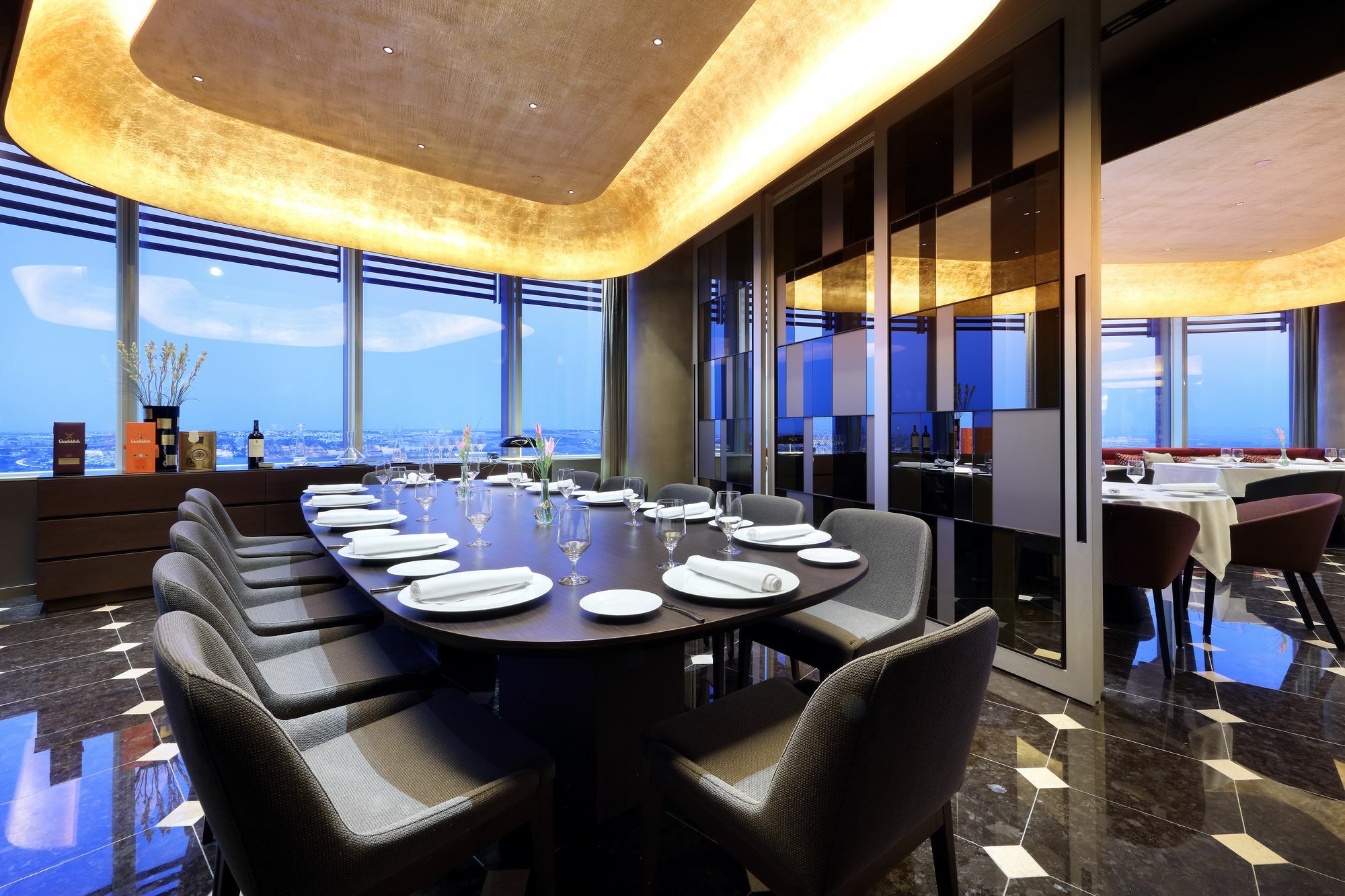 Eurostars Torre Sevilla Esterno foto The photo shows an elegant dining room with a long, dark wood table surrounded by plush chairs. The table is set with white plates and silverware, indicating it is ready for a meal. The room features large windows that offer a view of the outside, al