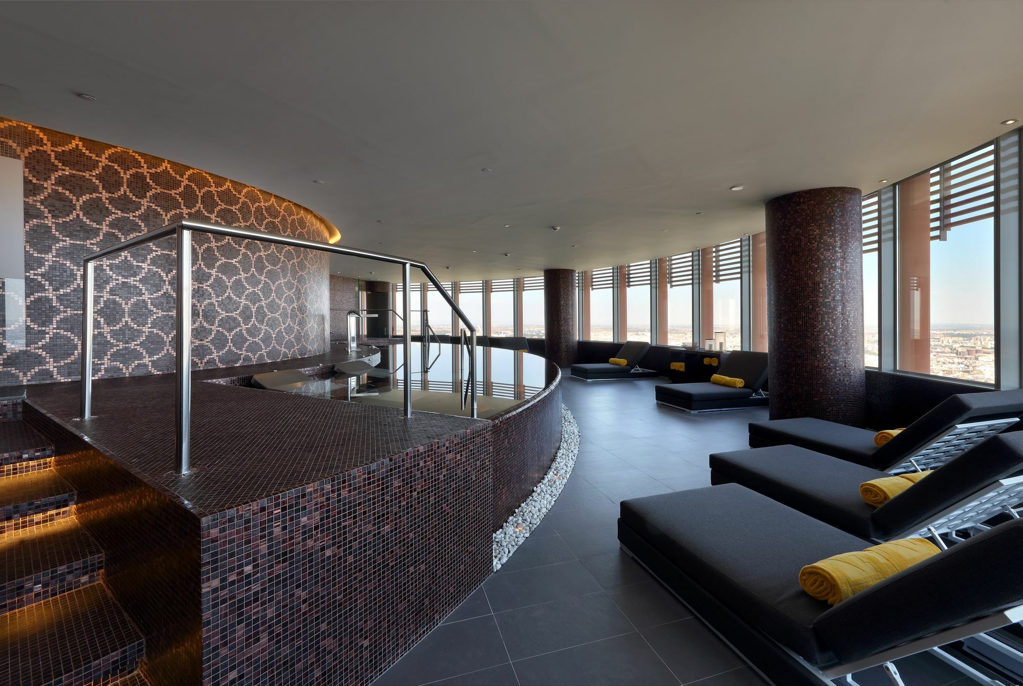 Eurostars Torre Sevilla Esterno foto The photo shows a modern spa or relaxation area with large windows that provide a panoramic view. The interior features a stylish design, highlighted by smooth, dark tiles and elegant stonework. There's a curved seating area with lounge chairs, accen