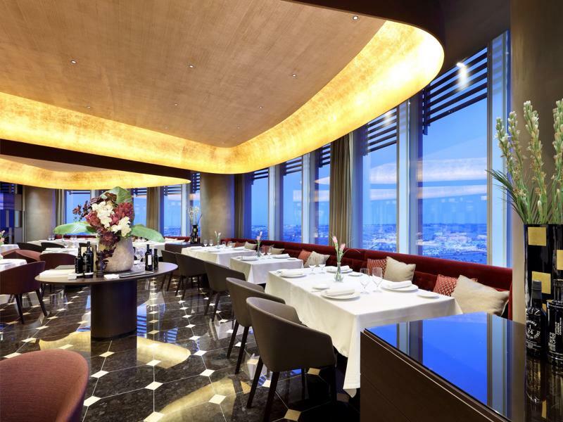 Eurostars Torre Sevilla Esterno foto The photo showcases an elegant restaurant interior, characterized by modern design elements. The space features a soft, curved ceiling illuminated with warm lighting, creating an inviting atmosphere. Tables are neatly set with white tablecloths and a