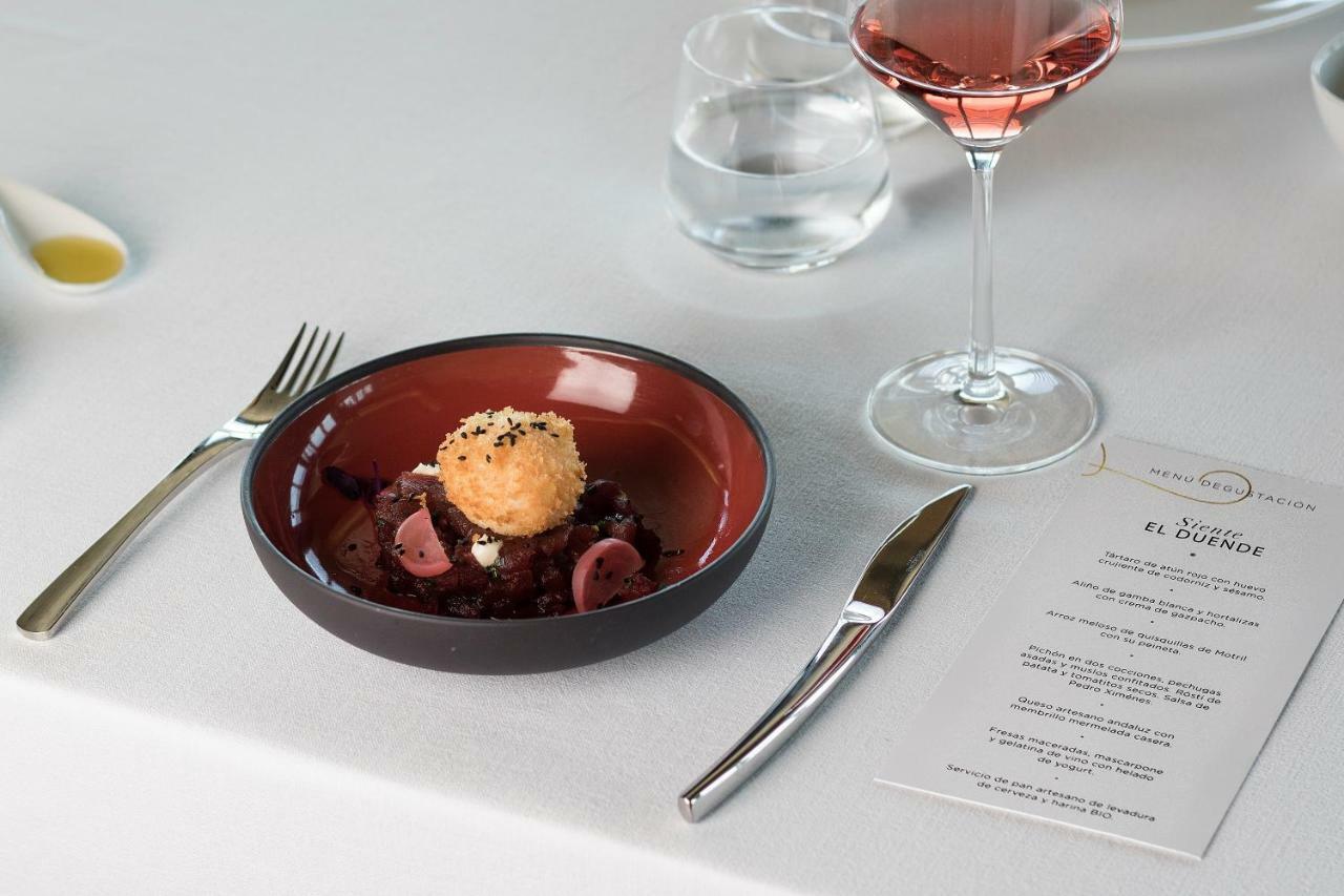 Eurostars Torre Sevilla Esterno foto The photo shows a beautifully arranged dining setting. In the center, there's a round bowl with a vibrant red interior, filled with a dish that features small pieces of meat or vegetables, garnished with a round, golden item that looks like a breaded