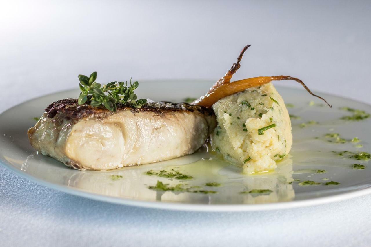 Eurostars Torre Sevilla Esterno foto The photo shows a plate of food featuring a piece of cooked fish, which appears to be topped with fresh herbs, possibly thyme. Next to the fish, there is a serving of mashed potatoes that has a creamy texture and is garnished with herbs. Additionally