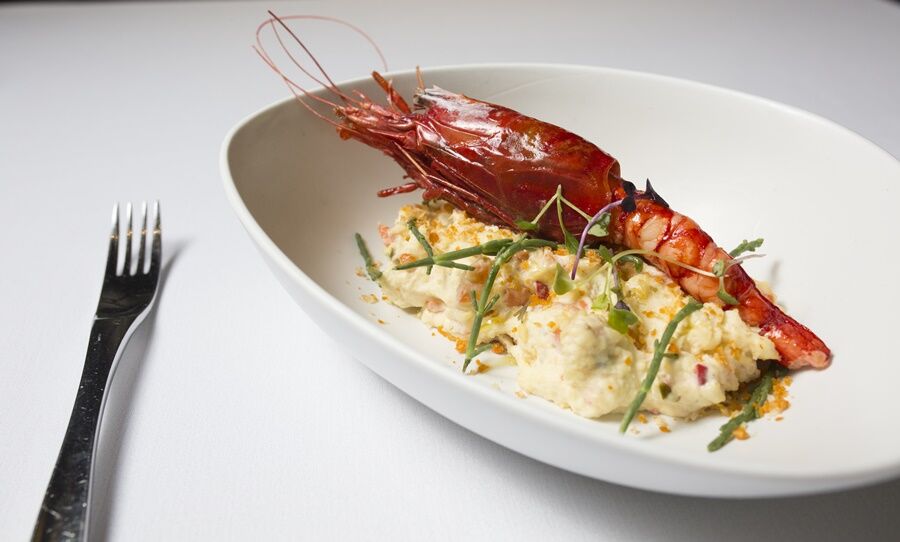 Eurostars Torre Sevilla Esterno foto The photo features a gourmet dish served in a white, oval bowl. It includes a large, grilled shrimp resting on a bed of creamy, textured food, likely a type of risotto or puree, which appears to include bits of vegetables. The dish is garnished with 